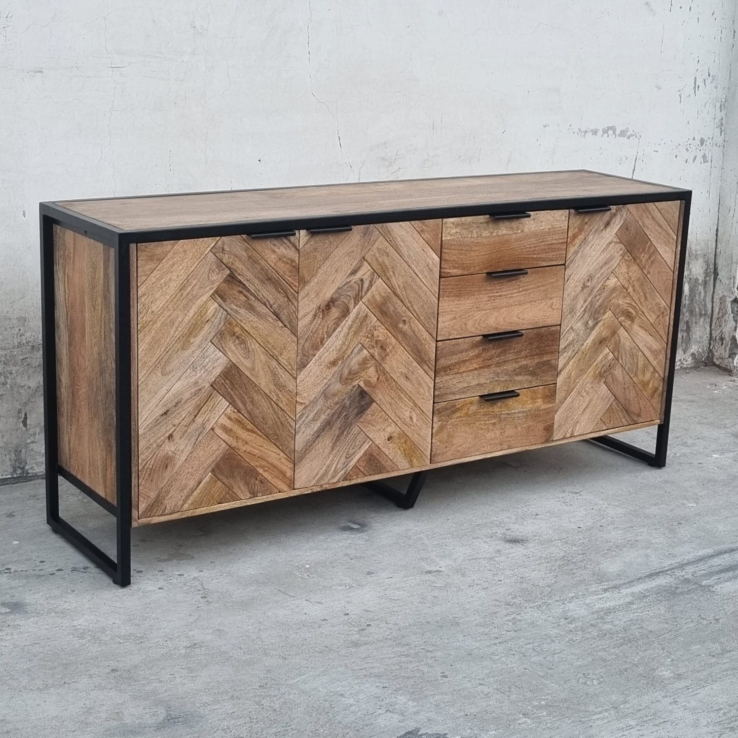 Ce buffet industriel moderne style herringbone Kukuu a été fabriqué à partir de bois massif de manguier et de métal. Il possède 4 tiroirs de rangement ainsi que 3 portes avec étagères et espaces de rangement. Mesures: 180 (L) x 46 (l) x 84 (H) cm. Kukuu, meubles industriels de qualité.