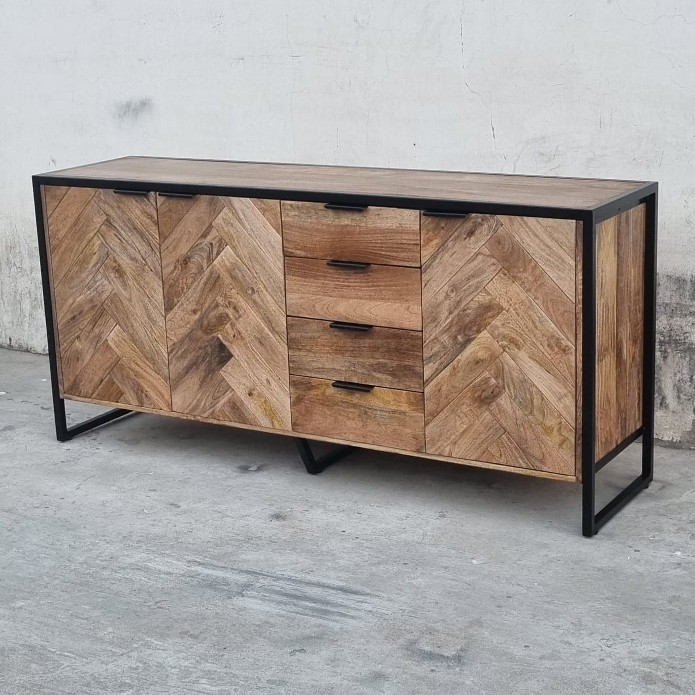 Ce buffet industriel moderne style herringbone Kukuu a été fabriqué à partir de bois massif de manguier et de métal. Il possède 4 tiroirs de rangement ainsi que 3 portes avec étagères et espaces de rangement. Mesures: 180 (L) x 46 (l) x 84 (H) cm. Kukuu, meubles industriels de qualité.