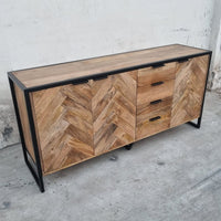 Ce buffet industriel moderne style herringbone Kukuu a été fabriqué à partir de bois massif de manguier et de métal. Il possède 4 tiroirs de rangement ainsi que 3 portes avec étagères et espaces de rangement. Mesures: 180 (L) x 46 (l) x 84 (H) cm. Kukuu, meubles industriels de qualité.