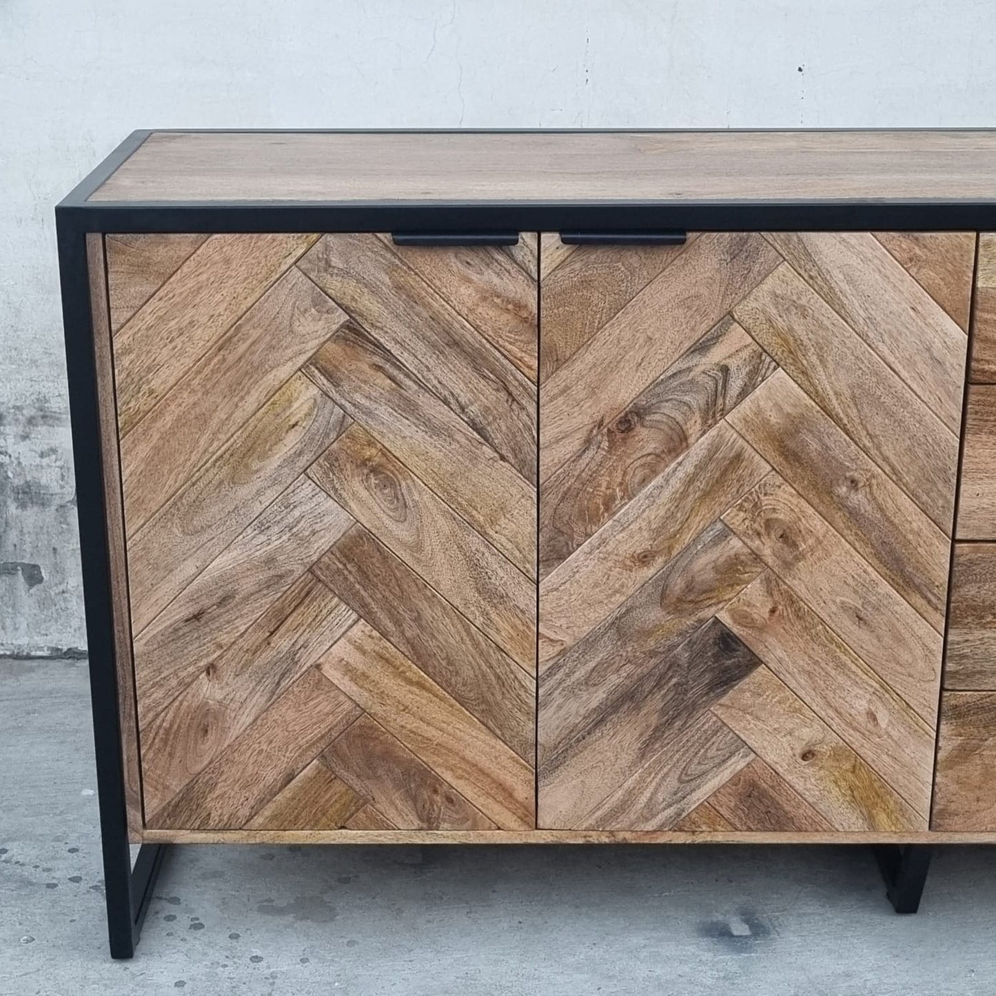 Ce buffet industriel moderne style herringbone Kukuu a été fabriqué à partir de bois massif de manguier et de métal. Il possède 4 tiroirs de rangement ainsi que 3 portes avec étagères et espaces de rangement. Mesures: 180 (L) x 46 (l) x 84 (H) cm. Kukuu, meubles industriels de qualité.