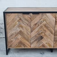 Ce buffet industriel moderne style herringbone Kukuu a été fabriqué à partir de bois massif de manguier et de métal. Il possède 4 tiroirs de rangement ainsi que 3 portes avec étagères et espaces de rangement. Mesures: 180 (L) x 46 (l) x 84 (H) cm. Kukuu, meubles industriels de qualité.