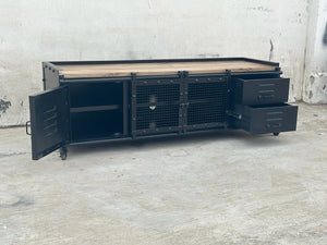 Ce meuble tv industriel Kukuu a été fabriqué à partir de bois massif de manguier et de métal. Il possède des étagères, 2 tiroirs, des portes coulissantes ainsi que des roulettes pour plus de praticité. Mesures: 180 (L) x 45 (l) x 55 (H) cm
